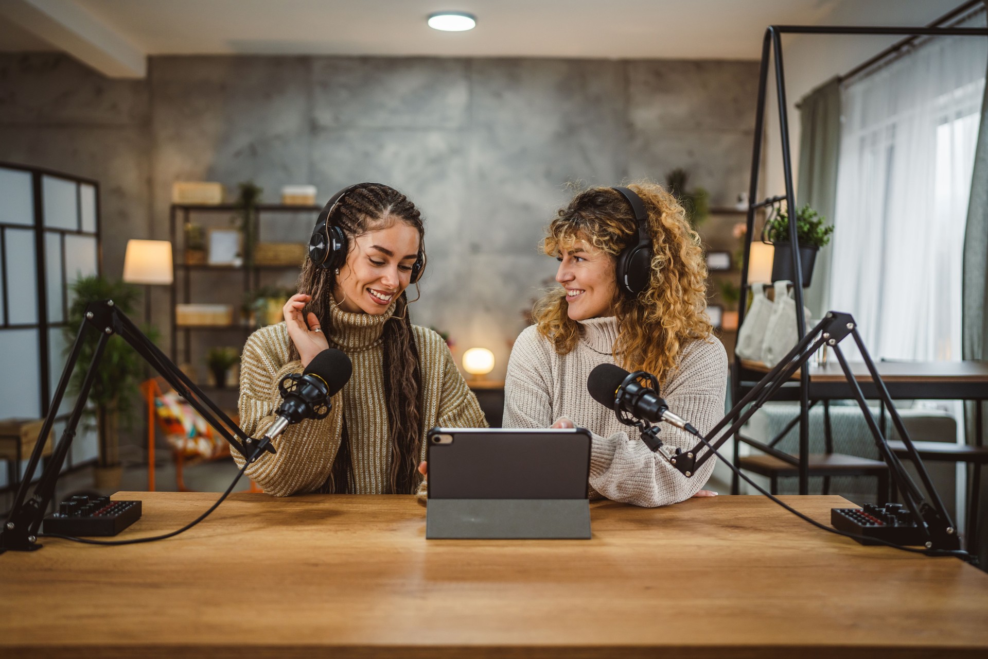Two young adult women stream audio podcast use microphone and tablet